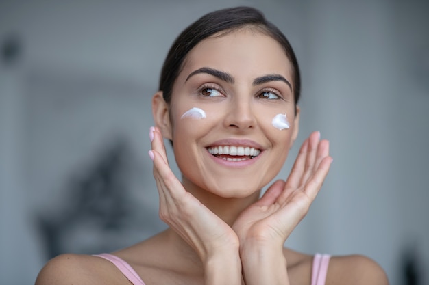 Mujer sonriente aplicar crema en las mejillas