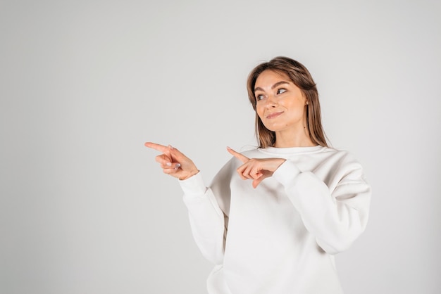 Mujer sonriente apuntando hacia un lado sobre fondo blanco.