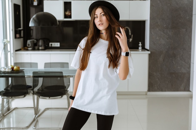 Mujer sonriente atractiva joven practicando yoga, haciendo ejercicio, vistiendo ropa deportiva, pantalón negro, interior de cuerpo entero, hogar. amplia cocina luminosa y sala de estar