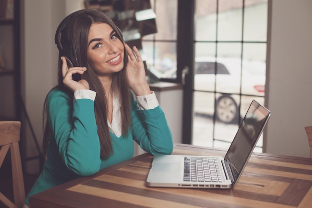 Una mujer sonriente con auriculares está sentada en la mesa con una laptop gris