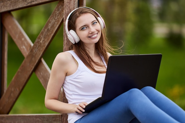 Mujer sonriente en auriculares con laptop afuera