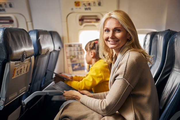 Mujer sonriente en un avión con una tableta