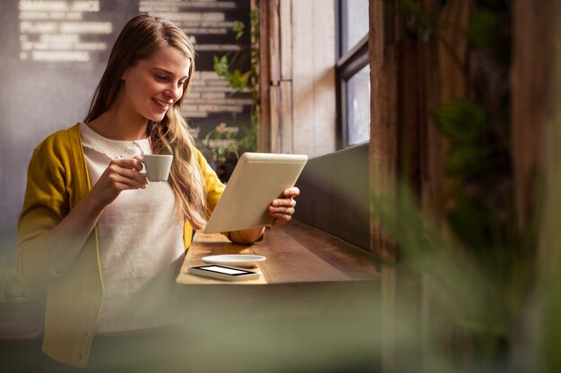 Mujer sonriente bebiendo café y usando tableta