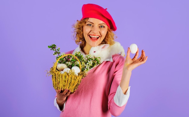 Mujer sonriente en boina de moda con conejo de pascua en los hombros y huevo de pascua en la mano