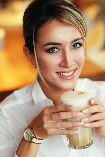 Mujer sonriente de buen humor con una taza de café sentada en la cafetería