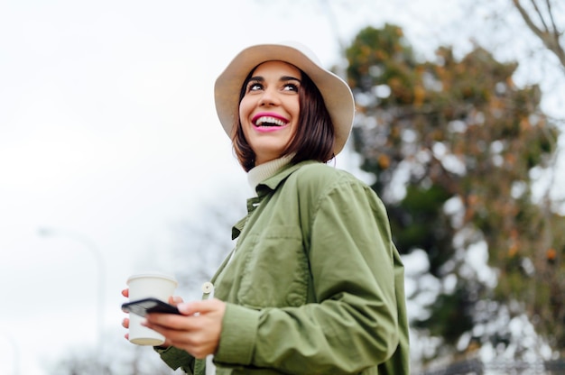 Mujer sonriente con café y smartphone en la calle