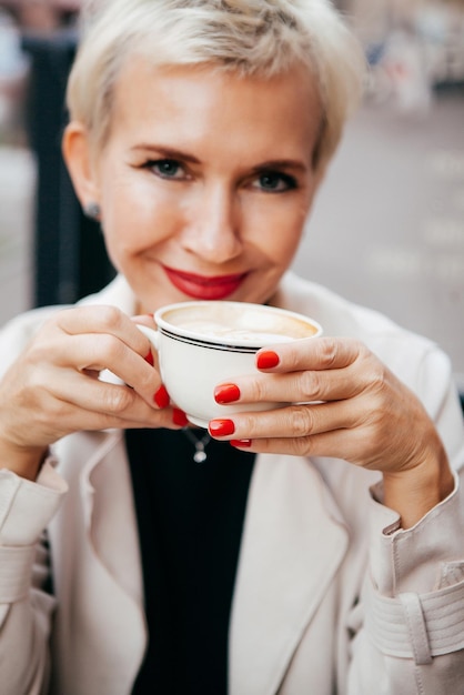 Mujer sonriente en café usa teléfono inteligente y bebe café