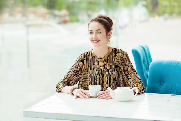 Mujer sonriente en la cafetería de la ciudad con una taza de té caliente y tetera