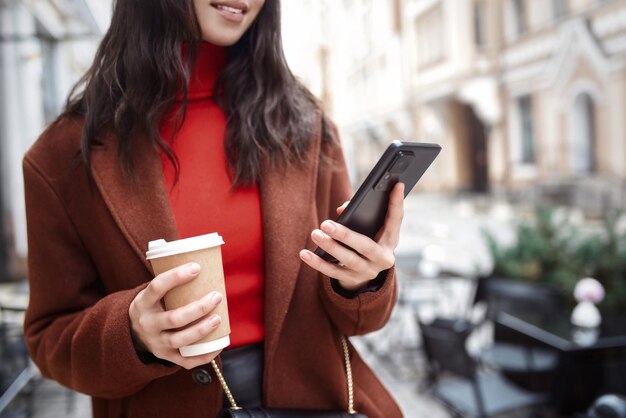 Mujer sonriente en la calle usando el teléfono y bebiendo escena de cultivo de café