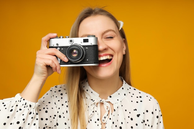 Mujer sonriente con cámara vintage en fondo naranja