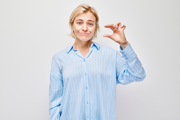 Mujer sonriente con camisa azul haciendo un pequeño gesto con sus dedos aislados en un fondo claro