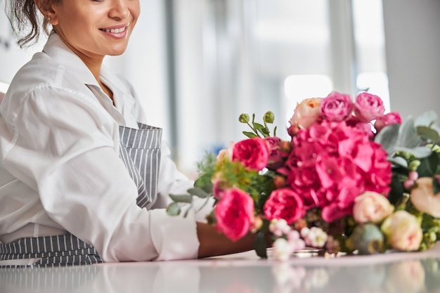 Mujer sonriente con una camisa blanca mirando un ramo de flores