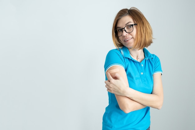 Mujer sonriente con una camiseta azul y gafas con una tirita en la mano se regocija de recibir una vacuna contra la infección por coronavirus Covid-19 Sputnik V