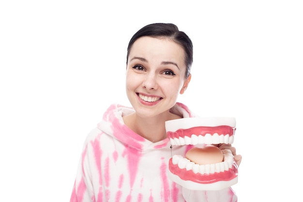 una mujer sonriente con una capucha rosa sostiene una mandíbula dental en su mano con fondo blanco