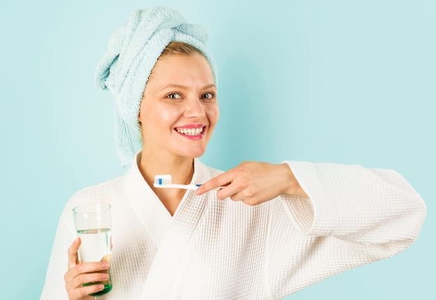 Mujer sonriente cepillarse los dientes usando un cepillo de dientes con pasta de dientes y un vaso de agua para el cuidado de los dientes