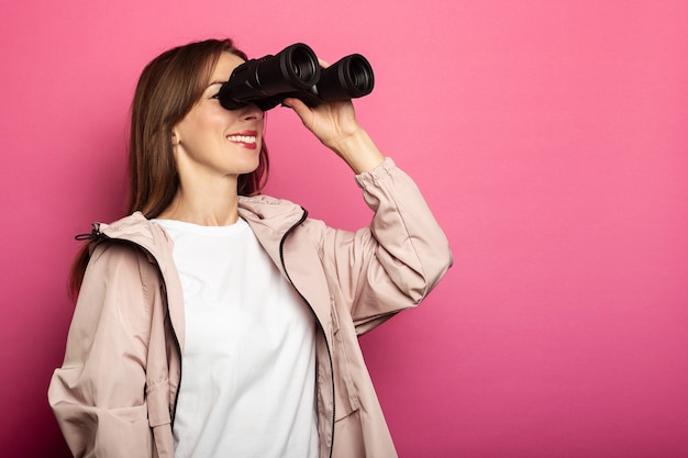 Mujer sonriente en chaqueta mirando a través de binoculares