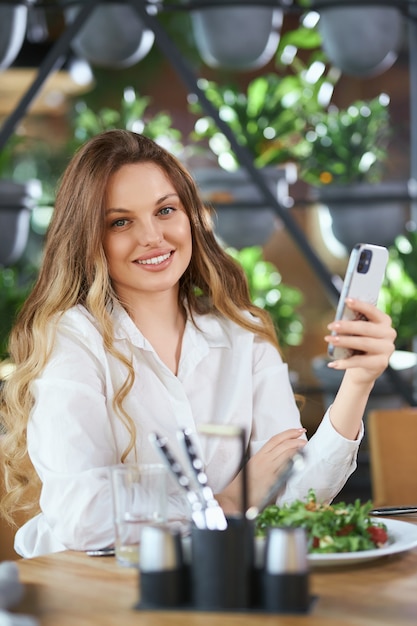 Mujer sonriente charlando con amigos por teléfono en el café