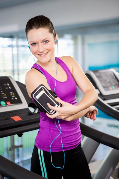 Mujer sonriente en la cinta con teléfono inteligente en el gimnasio