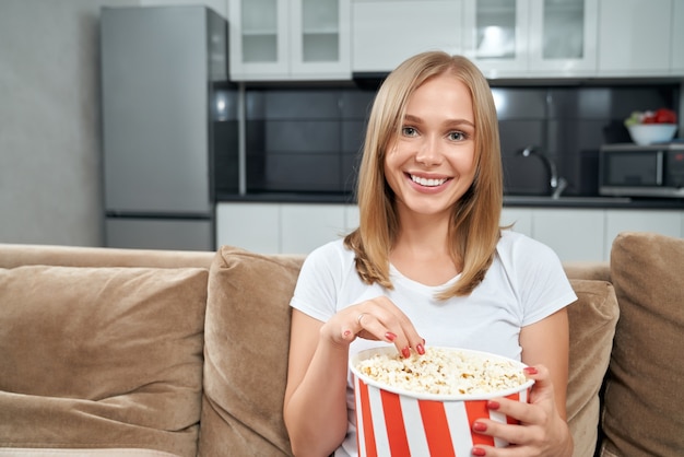 Mujer sonriente comiendo palomitas de maíz mientras está sentado en el sofá