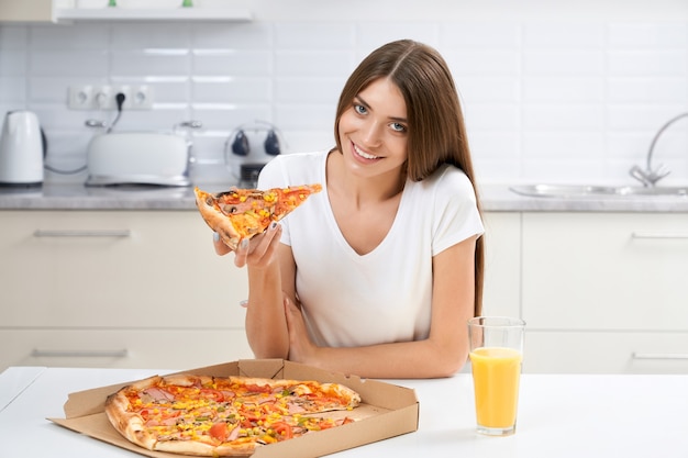 Mujer sonriente comiendo pizza sabrosa en la cocina