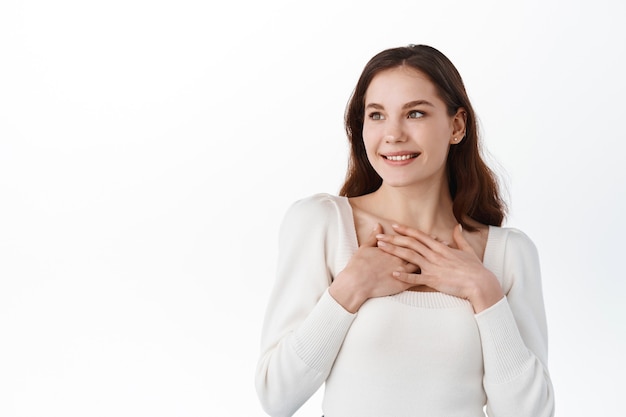 La mujer sonriente complacida mantiene las manos juntas sobre el pecho, expresa gratitud, mira a un lado, tocada con felicitaciones cordiales, hace un gesto de agradecimiento