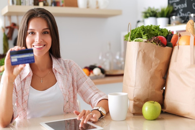 Mujer sonriente comprando en línea usando tableta y tarjeta de crédito en la cocina