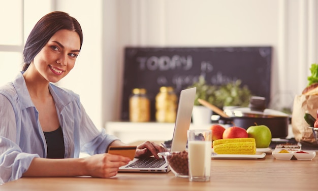 Mujer sonriente comprando en línea usando tableta y tarjeta de crédito en la cocina