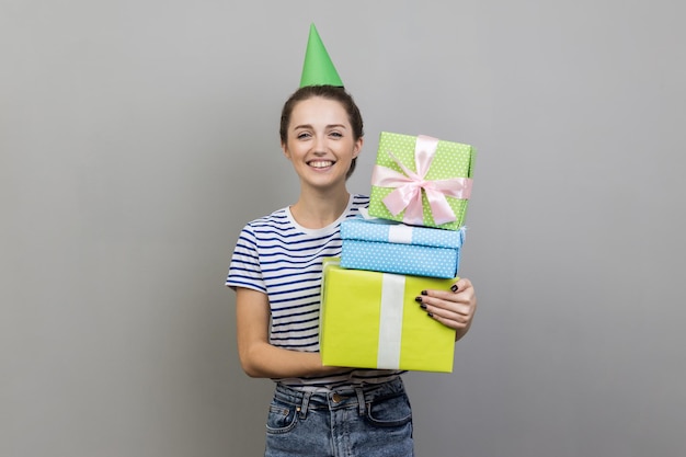 Mujer sonriente en cono de fiesta sosteniendo una pila de cajas presentes celebrando cumpleaños