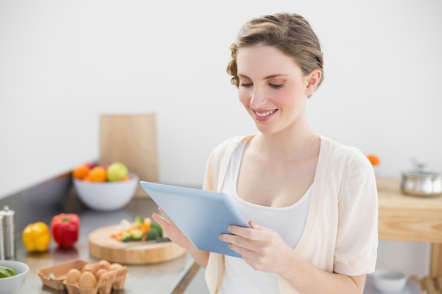 Mujer sonriente contenta que trabaja con su tableta en cocina