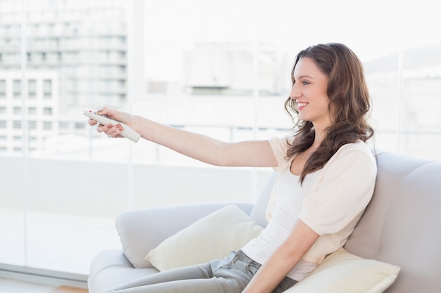 Mujer sonriente con control remoto sentado en el sofá