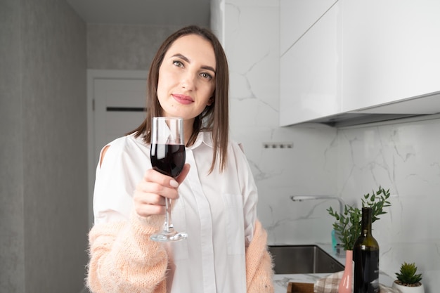 Mujer sonriente con una copa de vino tinto parada en la cocina