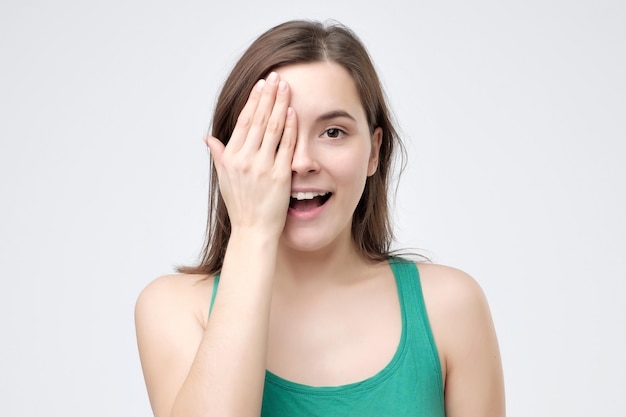 Mujer sonriente cubriendo un ojo con la mano mientras mira a la cámara