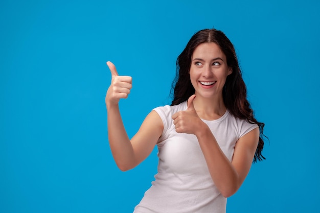 Mujer sonriente dando pulgares hacia arriba sobre fondo azul.