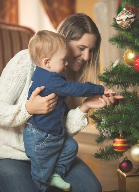 Mujer sonriente decorar el árbol de Navidad con su hijo de 10 meses