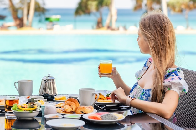 Mujer sonriente en desayuno americano bebiendo jugo de naranja junto a la piscina