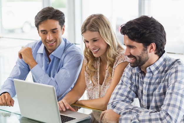 Mujer sonriente y dos hombres usando laptop