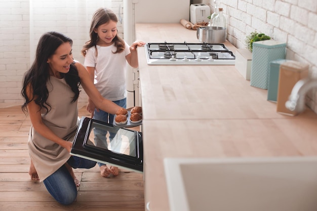 Foto mujer sonriente e hija pasando tiempo juntas cocinando muffins en la cocina