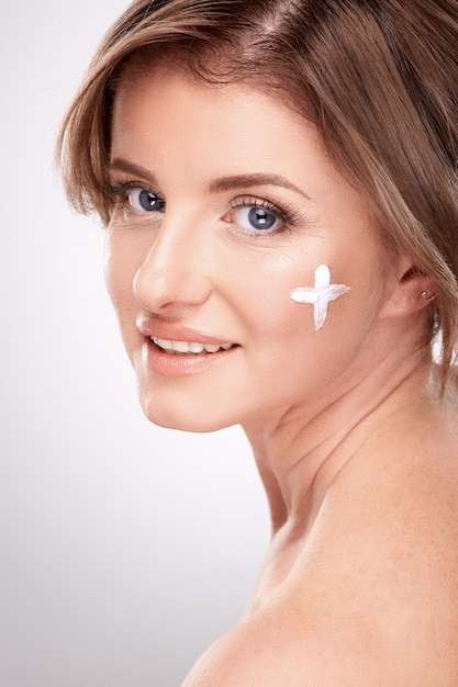 Mujer sonriente de edad media con maquillaje nude y hombros desnudos, concepto de fotografía de belleza, tratamiento de piel y arrugas, protección UV, uso de crema facial, plus en la cara.