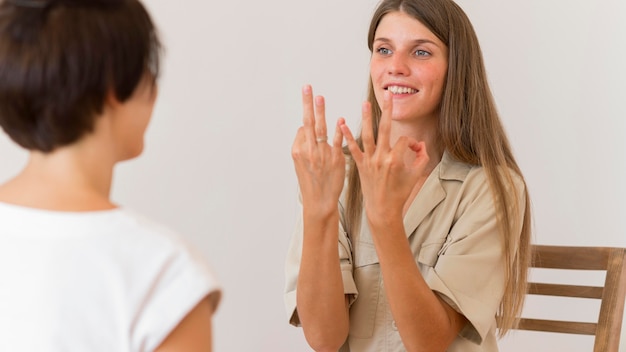 Foto mujer sonriente enseñando y mostrando lenguaje de señas a otra persona