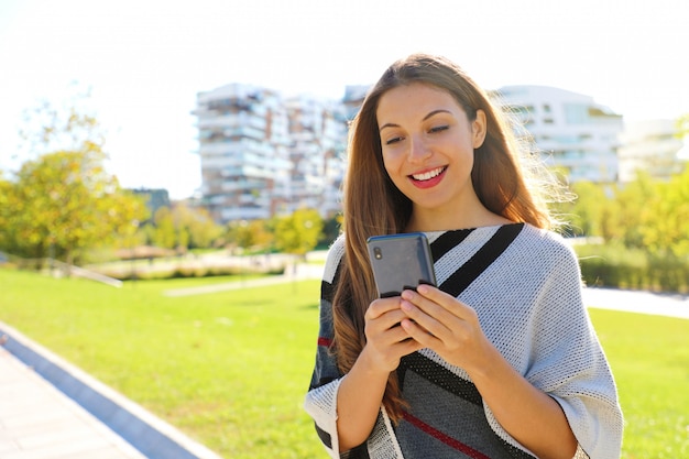 Mujer sonriente escribiendo en teléfonos inteligentes al aire libre en otoño invierno.