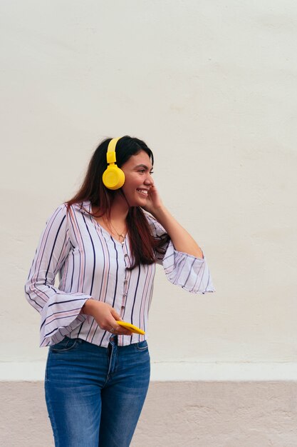 Mujer sonriente escuchando música junto a una pared blanca