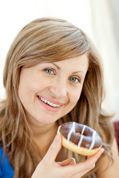 La mujer sonriente está comiendo un buñuelo en un sofá