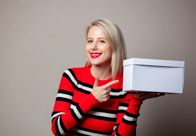 Mujer sonriente con estilo con caja de regalo blanca sobre pared gris