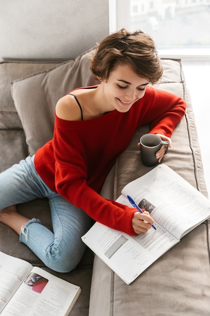 Mujer sonriente estudiando en un sofá en casa