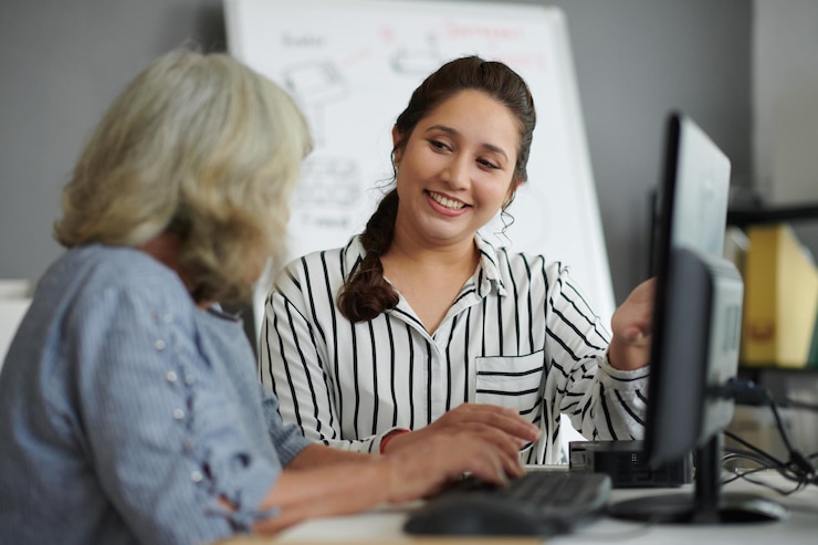 Foto mujer sonriente explicando a una mujer mayor cómo trabajar en la computadora