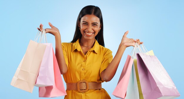 Mujer sonriente y feliz con bolsas de compras en el estudio para el marketing maquillaje en fondo azul cara de persona india y adicto a las compras para cosméticos de moda o venta sosteniendo regalos con las manos en el espacio