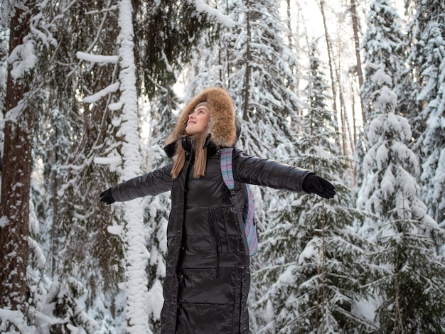 Una mujer sonriente feliz con una capucha en la cabeza abraza la naturaleza que la rodea.