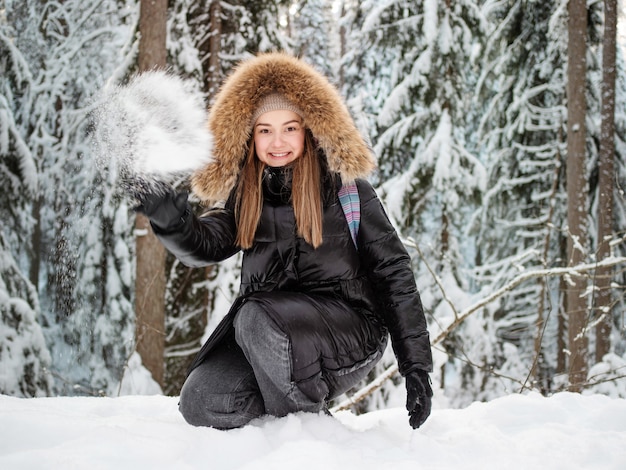 Una mujer sonriente feliz con una capucha de piel en la cabeza te arroja nieve