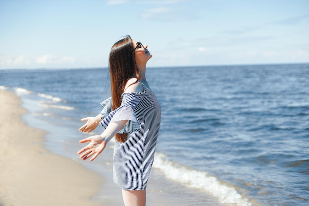 Foto mujer sonriente feliz en felicidad libre en la playa del océano de pie con las manos abiertas retrato de una modelo femenina morena en vestido de verano disfrutando de la naturaleza durante viajes vacaciones vacaciones al aire libre