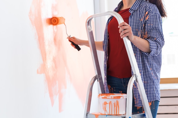 Mujer sonriente feliz pintando la pared interior de la casa nueva. Redecoración, renovación, reparación de apartamentos